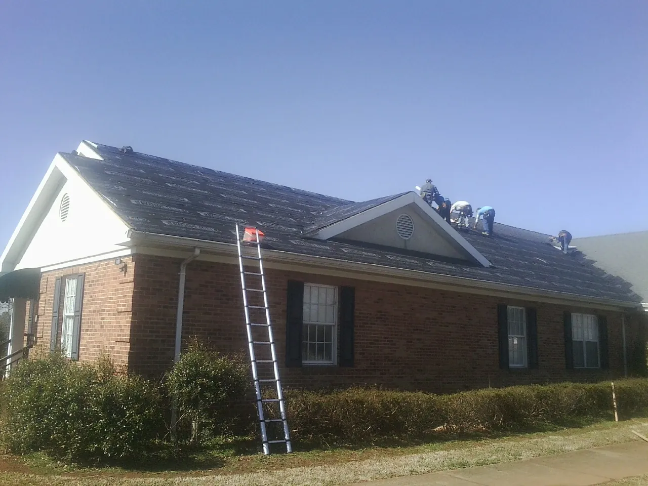 Crew tearing shingles off a brick ranch roof with a ladder set — Emergency Roof Repair work by our crew in Cavour
