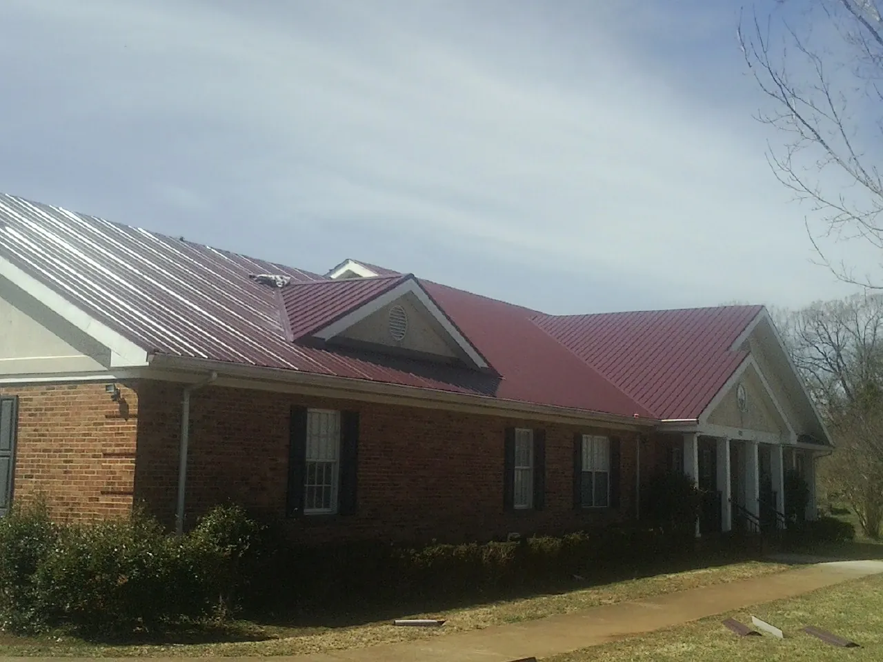 Red metal roof with gabled entries on a long brick building, from a Hail Damage Roof Repair job in Cavour