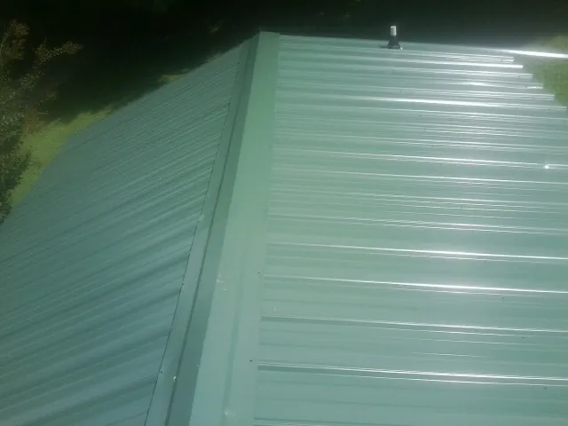 New green metal panels meeting at the ridge of a roof — Flat Roof Repair work by our crew in Cavour