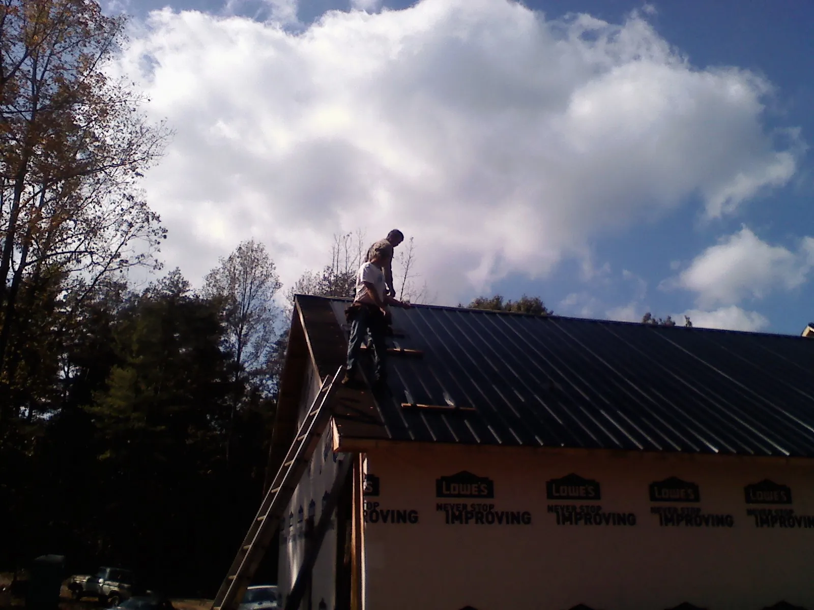 Roofer fastening dark metal panels high against a cloudy sky, from a Roof Inspection job in Cavour